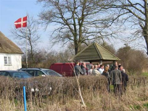 Vi st&aring;r p&aring; kanten til Nydam Mose og ser ud over omr&aring;det med de tidligere udgravningsfelter. I baggrunden Nydamselskabets informationshus og Nydamhuset.